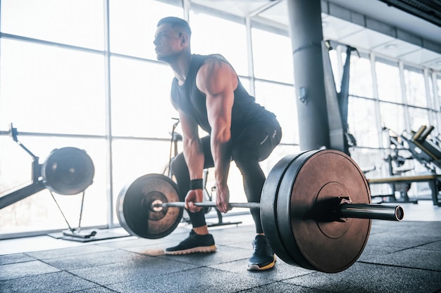 Jeune homme fort en vêtements sportifs faisant des exercices avec des poids lourds dans la salle de gym