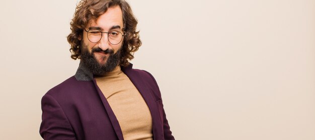 Jeune homme fou barbu à l'air heureux et amical, souriant et faisant un clin d'œil à vous avec une attitude positive contre le mur couleur plat