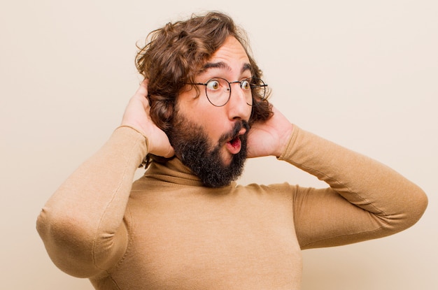 Jeune homme fou barbu, bouche ouverte, semblant horrifié et choqué par une terrible erreur, levant les mains sur sa tête