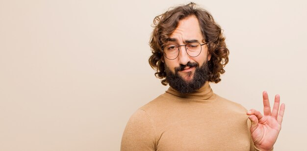 Jeune homme fou barbu à la recherche d'arrogant, réussi, positif et fier, pointant vers soi contre le mur de couleur plat