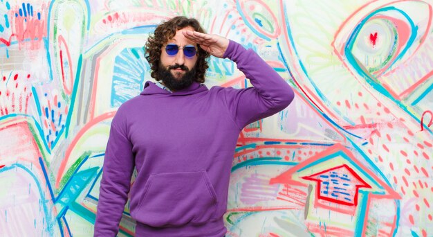 Jeune Homme Fou Barbu Saluant La Caméra Avec Un Salut Militaire Dans Un Acte D'honneur Et De Patriotisme, Respectant Le Mur De Graffitis