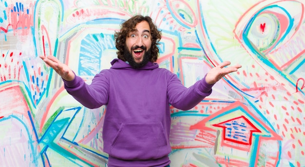 Jeune homme fou barbu souriant gaiement donnant un câlin de bienvenue chaleureux, amical, aimant, se sentant heureux et adorable sur le mur de graffitis