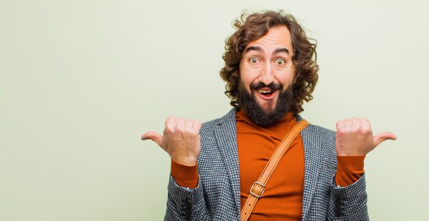 Jeune homme fou barbu souriant joyeusement et ayant l'air heureux, se sentant insouciant et positif avec les deux pouces contre une couleur plate