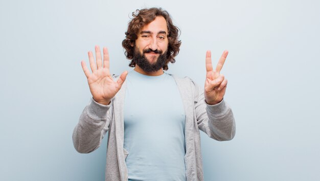 Photo jeune homme fou barbu souriant et regardant amicalement, montrant le numéro sept ou septième avec la main en avant, compte à rebours