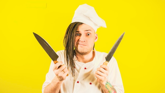 Jeune homme fou habillé en chef avec des couteaux sur fond jaune cuisinier mâle fou