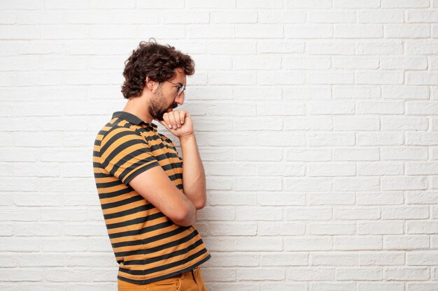 Jeune homme fou ou idiot, gesticulant et exprimant des émotions sur fond de mur de briques