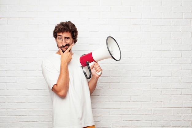 Jeune homme fou avec un mégaphone contre le mur de briques.