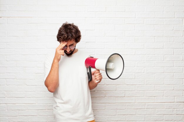 Jeune homme fou avec un mégaphone contre le mur de briques.