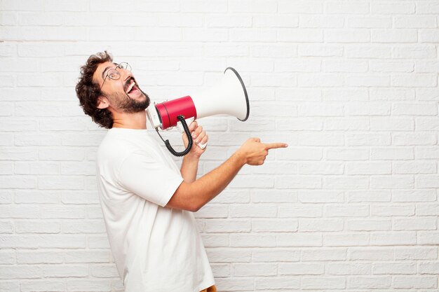 Jeune homme fou avec un mégaphone contre le mur de briques.