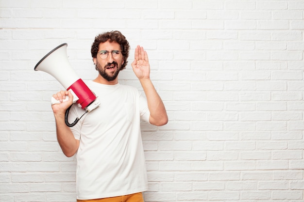 Jeune homme fou avec un mégaphone contre le mur de briques.