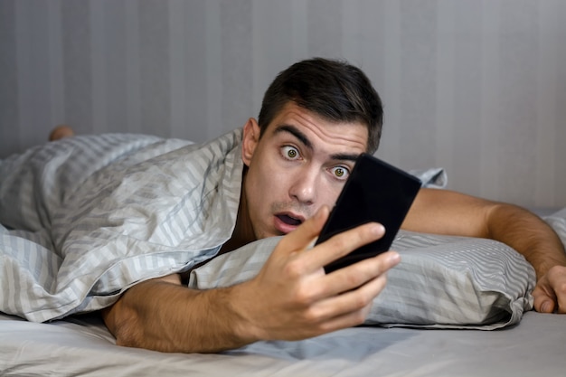 Jeune homme frustré et stressé est en retard. Il se réveille, regarde un smartphone et est sous le choc.