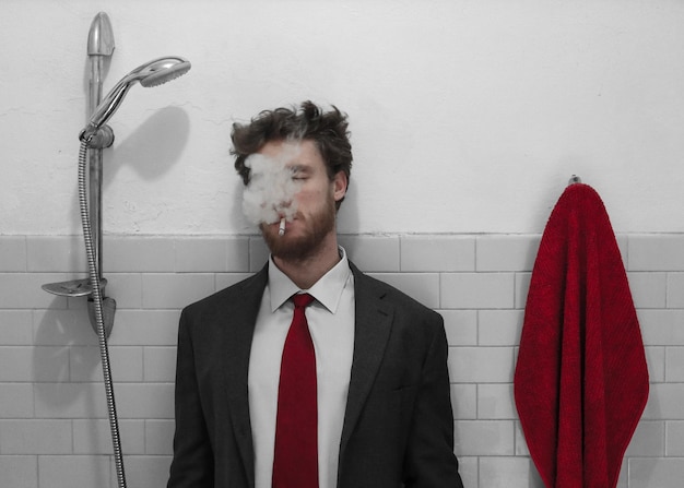 Photo un jeune homme fume une cigarette alors qu'il se tient contre le mur.