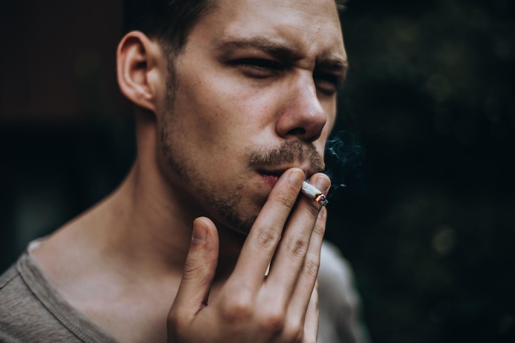 Photo un jeune homme fume une cigarette à l'extérieur.