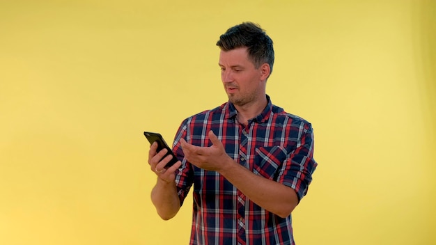 Photo un jeune homme gai est très ravi de quelque chose qui regarde sur un smartphone, il y a un fond jaune