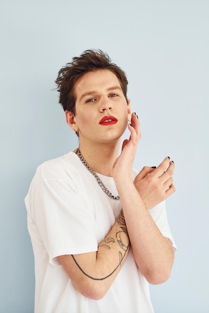 Jeune homme gay est debout dans le studio et pose pour un appareil photo Lèvres en rouge à lèvres
