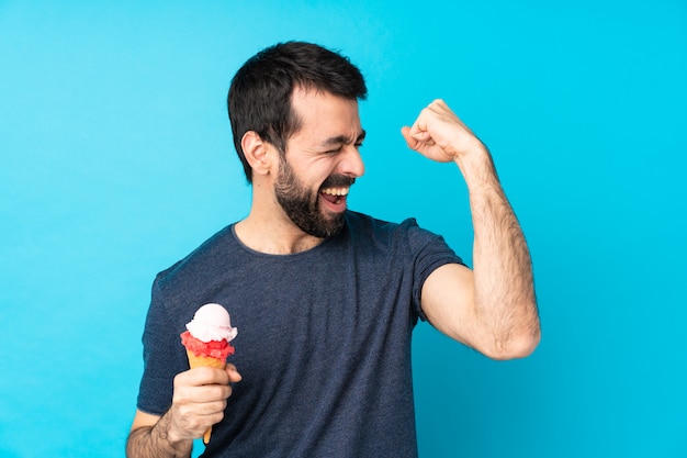 Jeune homme avec une glace au cornet sur un mur bleu isolé célébrant une victoire