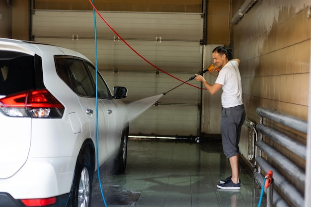 Jeune homme de grande taille écrasant sa voiture par un tuyau d'arrosage