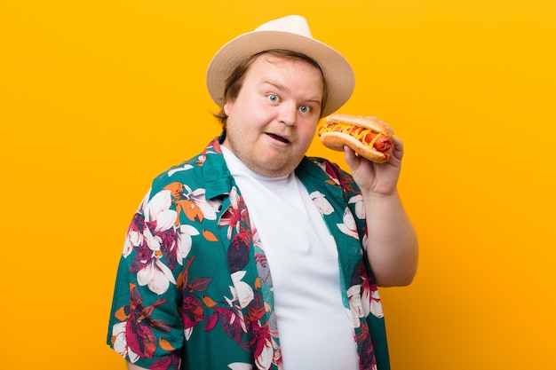 Jeune homme de grande taille avec un hot-dog contre un mur plat