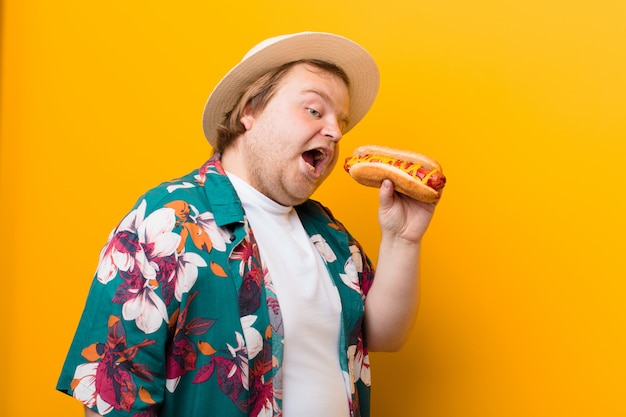 Jeune homme de grande taille avec un hot-dog contre un mur plat