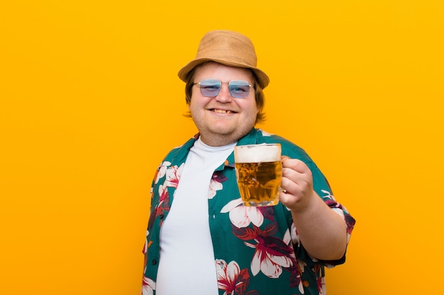 Jeune homme de grande taille avec une pinte de bière contre un mur plat