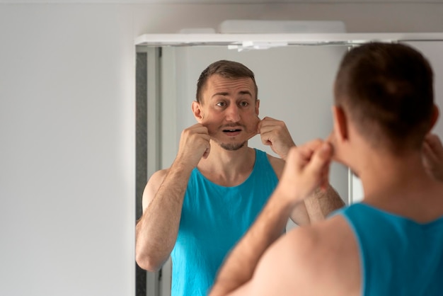 Jeune homme grimace et fait des grimaces à son reflet dans le miroir de la salle de bain