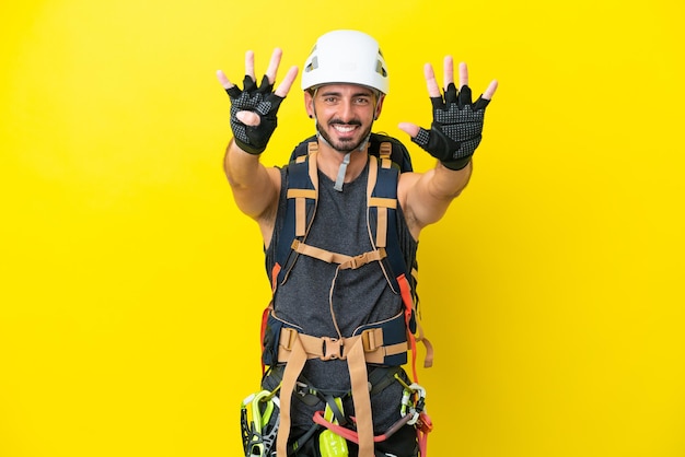 Jeune homme grimpeur caucasien isolé sur fond jaune comptant neuf avec les doigts