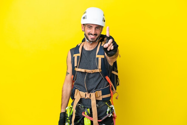 Jeune homme grimpeur caucasien isolé sur fond jaune montrant et levant un doigt