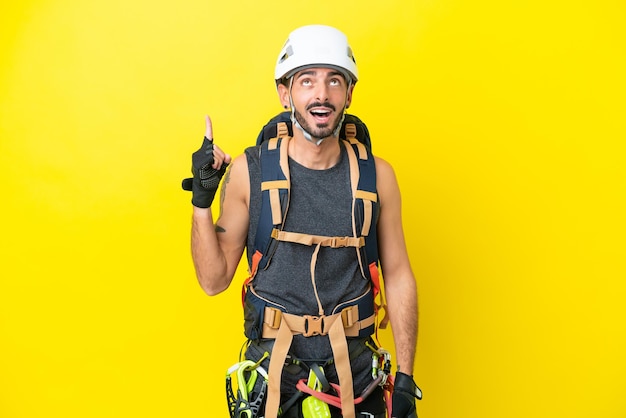 Jeune homme grimpeur caucasien isolé sur fond jaune pointant vers le haut et surpris