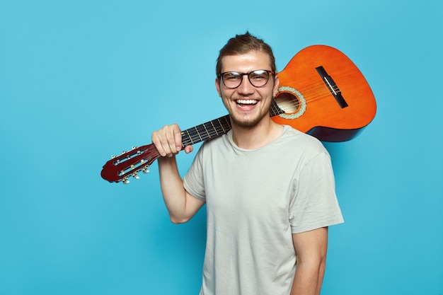 Photo jeune homme, à, guitare acoustique, sur, épaule, sourire, sur, mur bleu