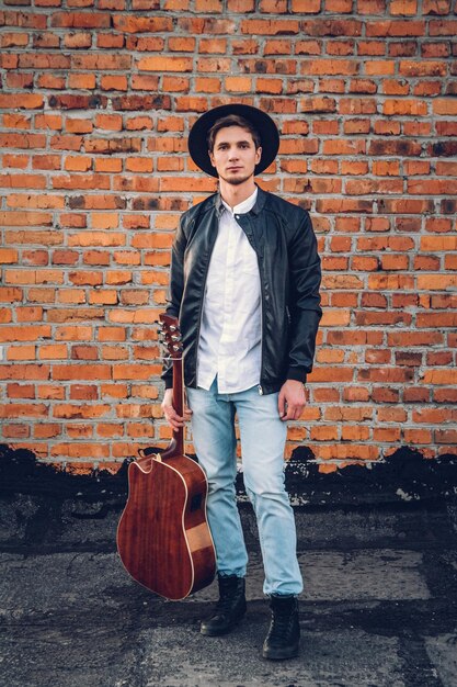 Photo jeune homme avec une guitare sur le fond d'un mur de briques