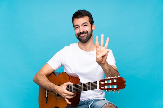 Jeune homme avec une guitare heureuse et comptant trois avec les doigts