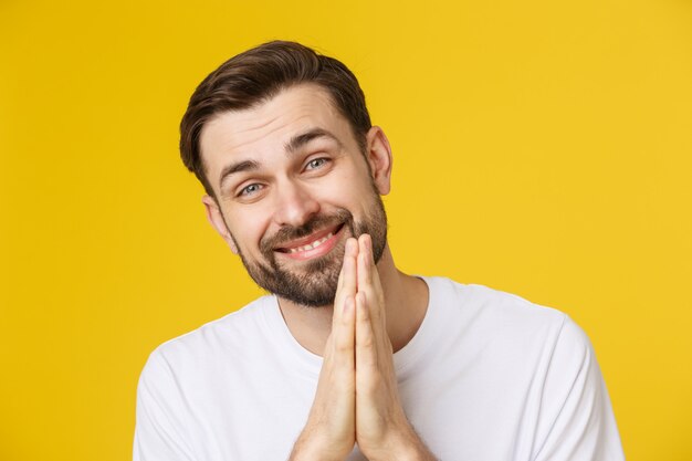 Jeune homme habillé avec désinvolture isolé sur fond jaune, ayant mis les mains ensemble dans la prière ou la méditation, l'air détendu et calme.