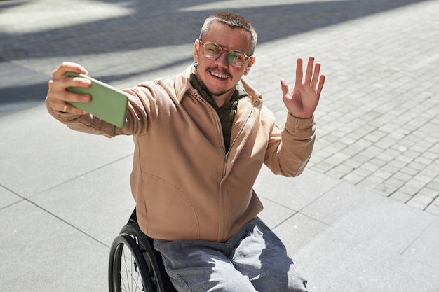 Jeune homme handicapé ayant un appel vidéo sur son smartphone lors de sa promenade dans la ville