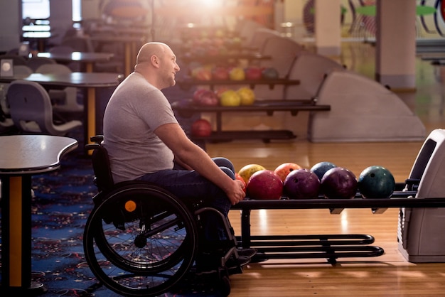 Photo jeune homme handicapé en fauteuil roulant à jouer au bowling dans le club