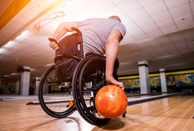 Jeune homme handicapé en fauteuil roulant à jouer au bowling dans le club