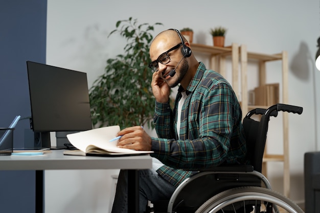 Jeune homme handicapé en fauteuil roulant travaillant à sa table de travail avec un casque sur