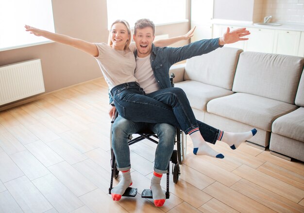 Jeune homme handicapé et inclusif tenant une copine à genoux. Ils sourient et posent devant la caméra. Couple heureux gai.