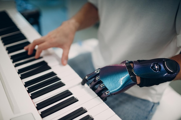 Un jeune homme handicapé joue sur un synthétiseur électronique de piano avec une main prothétique artificielle dans un magasin de musique.