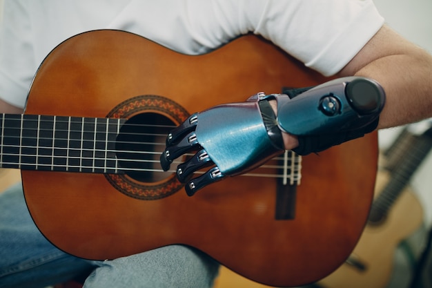 Le jeune homme handicapé avec la main prothétique artificielle joue sur des cordes de guitare au magasin