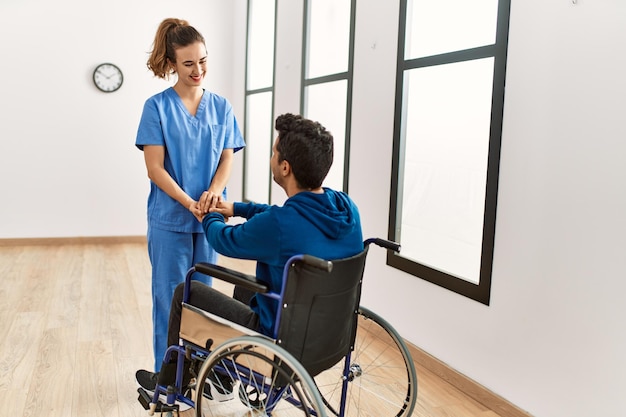 Un jeune homme handicapé et un physiothérapeute souriants, heureux, se serrant la main à la clinique.