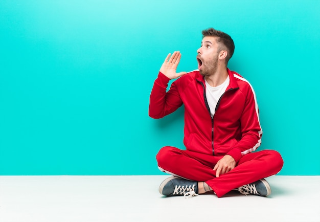 Jeune homme handosme criant fort et en colère pour copier l'espace sur le côté, avec la main à côté de la bouche contre le mur de couleur plat