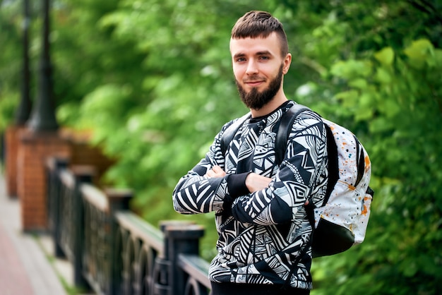 jeune homme avec une herse sourit. Les mains croisées et une mallette à l'arrière.