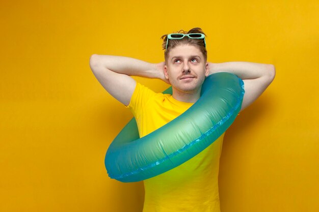 Un jeune homme heureux avec un anneau de natation gonflable en vacances se trouve sur un fond jaune et rêve