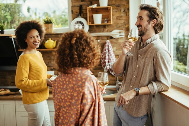 Photo jeune homme heureux buvant du vin et parlant avec ses amies dans la cuisine