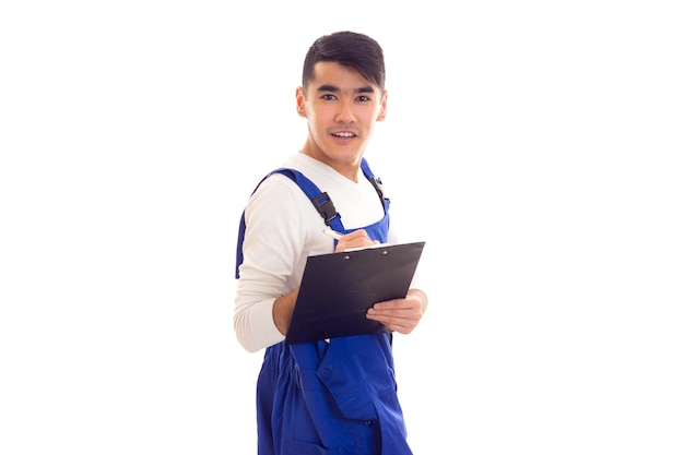 Jeune homme heureux en chemise blanche et combinaison bleue tenant un stylo blanc et un dossier noir