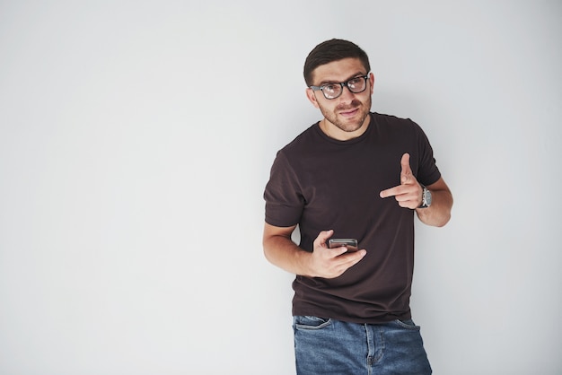 Jeune homme heureux décontracté habillé avec un téléphone intelligent sur fond blanc.