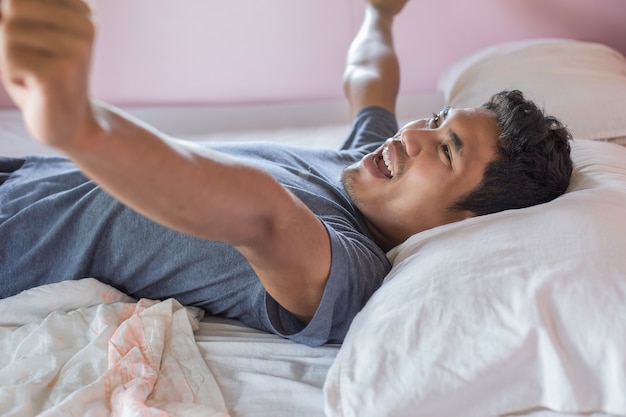 Jeune homme heureux se réveiller sur le lit