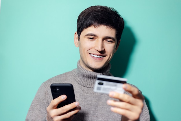 Jeune Homme Heureux Avec Smartphone Et Carte De Crédit à La Main Sur Le Mur De Couleur Aqua Menthe.