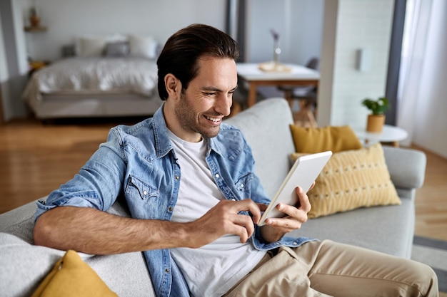 Jeune homme heureux surfant sur le net sur le pavé tactile tout en se relaxant à la maison