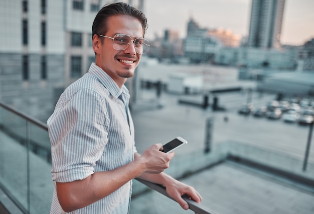 Jeune homme heureux tenant un téléphone à la main et souriant.